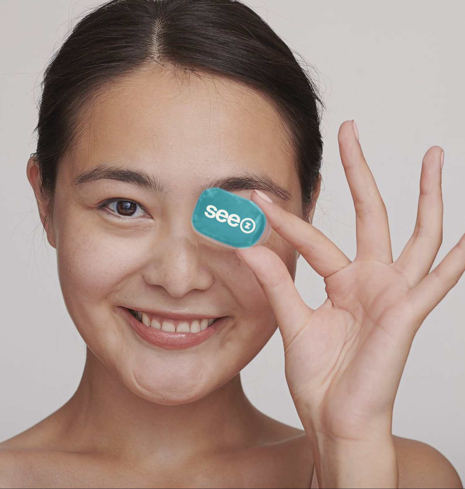 A smiling patient holding a See Z lens pack beside her eye